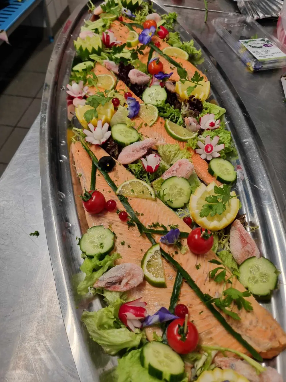 Saumon entier dressé sur plat, citron, concombre et fleurs comestibles